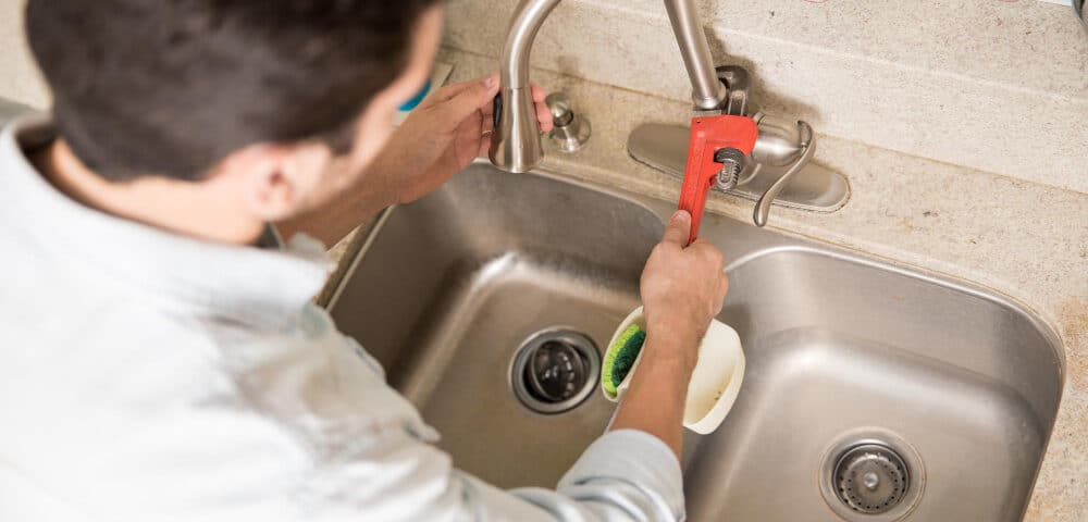 male plumber using wrench tighten water faucet kitchen seen up close