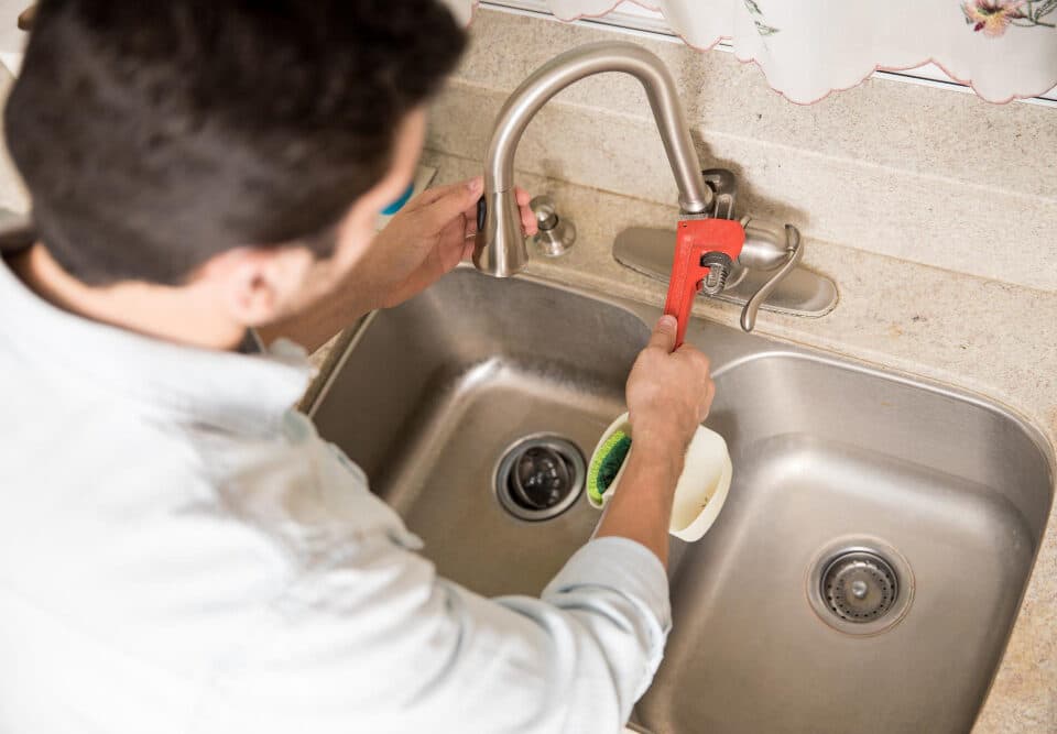 male plumber using wrench tighten water faucet kitchen seen up close