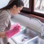 Woman Using Plunger In Kitchen Sink